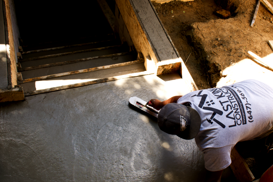 Crew smoothing concrete near a foundation staircase